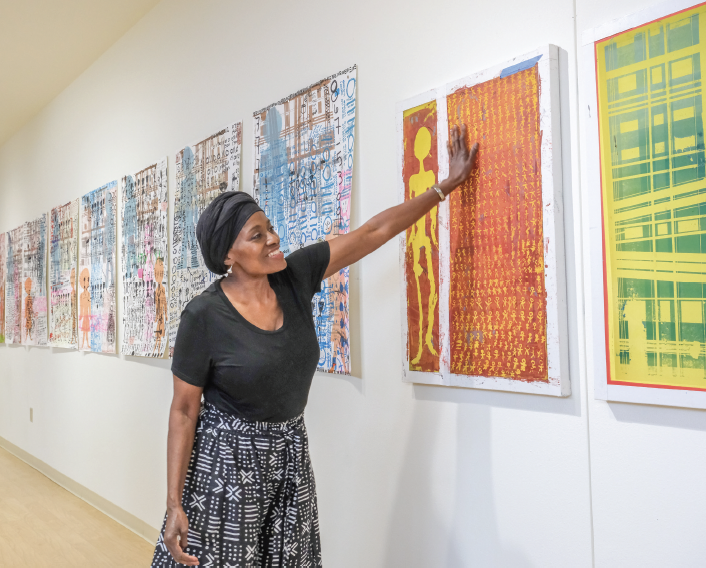 Artist Michelle Johnson points at an art piece on the wall in the “Tally Up!” art show on TR Campus.